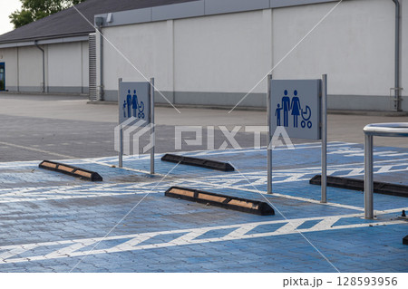 Spacious designated parking spots with blue ground markings and family stroller signs at an empty commercial supermarket lot, symbolizing convenient accessibility Spacious designated parking spots with blue ground markings and family stroller signs at an empty commercial supermarket lot, symbolizing convenient accessibility 128593956