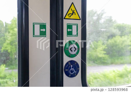 Train door panel with essential safety warning signs, clear exit arrows, and passenger assistance buttons for public transportation access and guidance 128593968