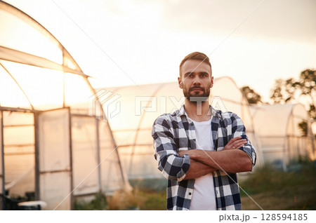 Young man on agricultural field near the greenhouse that is behind 128594185