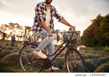 Handsome man in casual clothes is with bicycle on the agricultural field near greenhouse Handsome man in casual clothes is with bicycle on the agricultural field near greenhouse 128594207