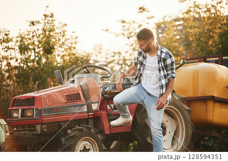 Farmer is casual clothes is standing near little tractor outdoors 128594351