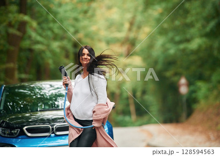 Cheerful beautiful woman is near blue car outdoors 128594563