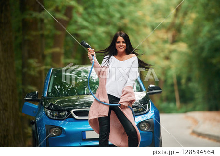 Cheerful beautiful woman is near blue car outdoors 128594564