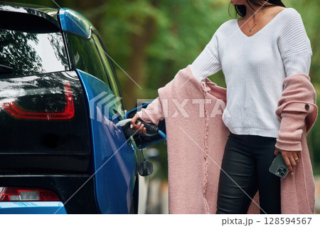 Woman is putting charger into the socket of electric automobile 128594567