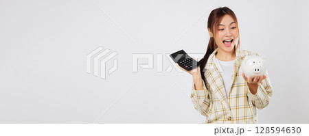 Excited woman manages saving plan by checking numbers on calculator, then reviewing on second calculator, using piggybank and tax strategy for smart finance. isolated studio white background Excited woman manages saving plan by checking numbers on calculator, then reviewing on second calculator, using piggybank and tax strategy for smart finance. isolated studio white background 128594630