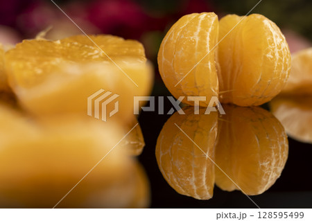 the reflection of a white orange citrus tangerine in a black mirror surface, a beautiful peeled and juicy tangerine on a black mirror 128595499