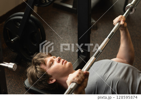 Young caucasian man doing bench press exercise with barbell in modern gym. Chest workout. 128595874