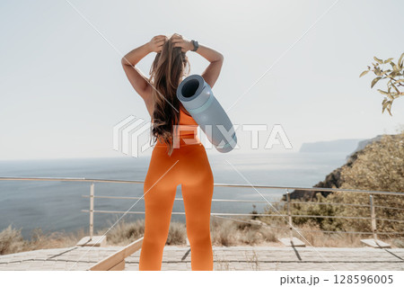 Woman in Orange Sportswear with Yoga Mat on a Clifftop 128596005