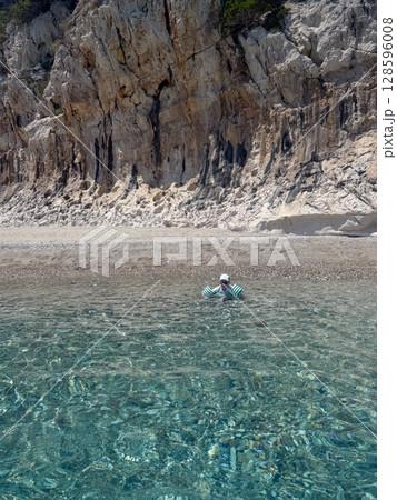Boy with floaties enjoying transparent sea water near stony beach and high cliffs in Sardinia, Italy. Cala luna 128596008