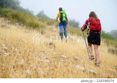 Hikers Ascending Foggy Mountain Trail Amid Wild Grass and Nature Hikers Ascending Foggy Mountain Trail Amid Wild Grass and Nature 128596074