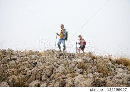Hikers Exploring Rocky Terrain with Trekking Poles in Misty Mountains Hikers Exploring Rocky Terrain with Trekking Poles in Misty Mountains 128596097