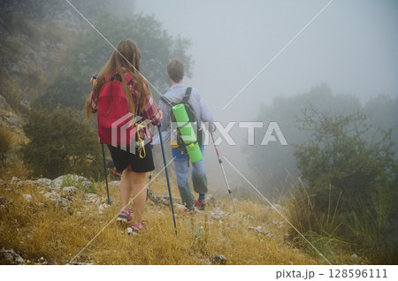 Couple Hiking Through Misty Mountain Trail with Backpacks and Trekking Poles Couple Hiking Through Misty Mountain Trail with Backpacks and Trekking Poles 128596111