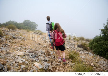 Hikers Traversing a Rocky Path in a Foggy Mountain Landscape 128596139