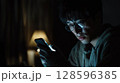 Man Gazes at Smartphone Screen in Dimly Lit Room During Late Night Hours 128596385