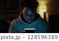 Young Person Absorbed in Smartphone Use in a Dimly Lit Room During Evening Hours 128596389