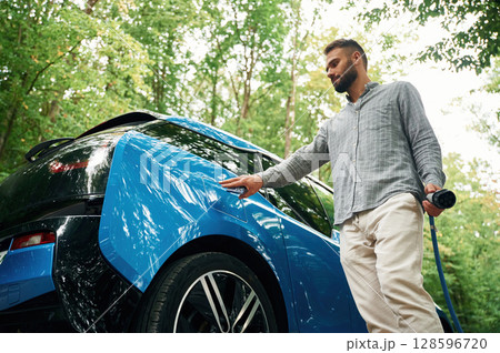 Young man is putting charger into the socket of electric automobile 128596720