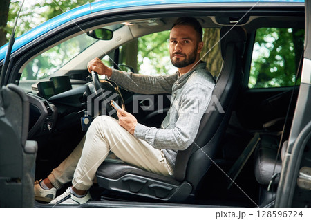 Beautiful young man is sitting in the blue car outdoors Beautiful young man is sitting in the blue car outdoors 128596724