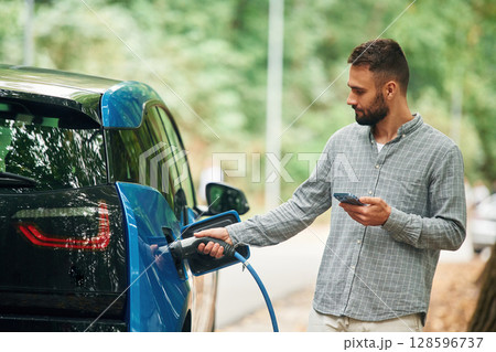 Young man is putting charger into the socket of electric automobile Young man is putting charger into the socket of electric automobile 128596737