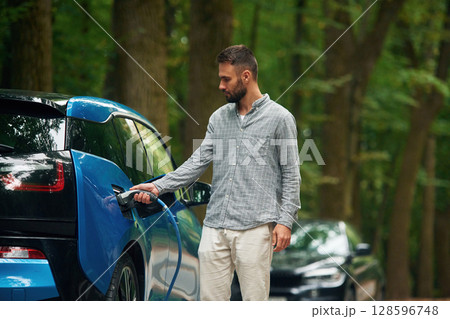 Young man is putting charger into the socket of electric automobile Young man is putting charger into the socket of electric automobile 128596748