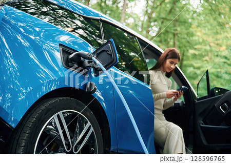 Young woman is sitting in electric automobile that is charging Young woman is sitting in electric automobile that is charging 128596765