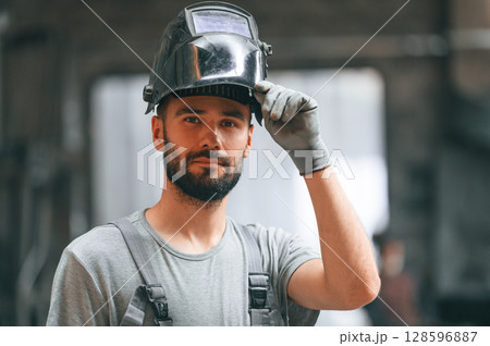 Welder man in safety helmet. Young factory worker in grey uniform Welder man in safety helmet. Young factory worker in grey uniform 128596887