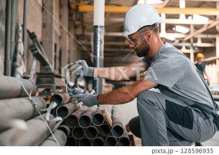 Sitting and working. Young man at the factory in grey uniform Sitting and working. Young man at the factory in grey uniform 128596935