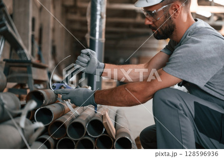 Sitting and working. Young man at the factory in grey uniform 128596936