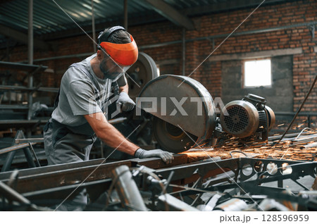Process of cutting the metal. Young factory worker in grey uniform 128596959