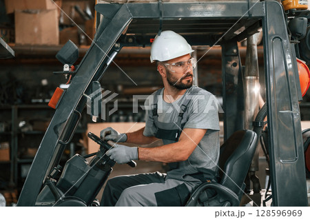 Driving the forklift. Young factory worker in grey uniform 128596969