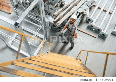 Climbing up on the ladder. Young factory worker in grey uniform 128596994