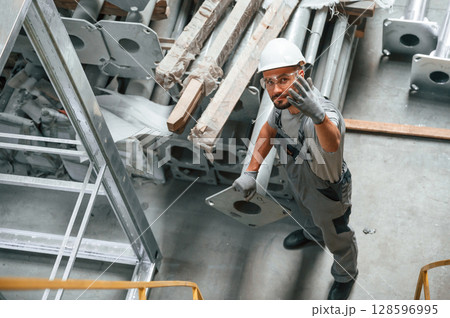 Making gesture by hands. Young factory worker in grey uniform 128596995