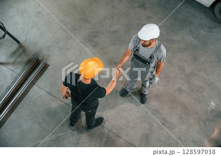 Top view of two factory workers that are standing and making handshake, business deal Top view of two factory workers that are standing and making handshake, business deal 128597038