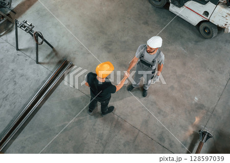 Top view of two factory workers that are standing and making handshake, business deal Top view of two factory workers that are standing and making handshake, business deal 128597039