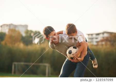 Holding professional soccer ball. Father and little son are playing and having fun outdoors 128597099