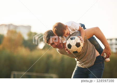 Holding professional soccer ball. Father and little son are playing and having fun outdoors Holding professional soccer ball. Father and little son are playing and having fun outdoors 128597100