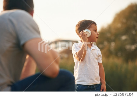 With string can phone. Father and little son are playing and having fun outdoors With string can phone. Father and little son are playing and having fun outdoors 128597104