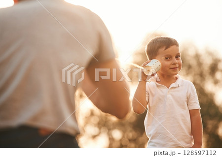 Fun, holding and using string can phone. Father and little son are playing outdoors Fun, holding and using string can phone. Father and little son are playing outdoors 128597112