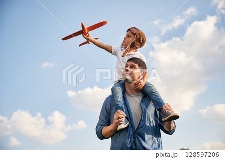 With aviator glasses, playing with toy plane. Father and little son are having fun outdoors With aviator glasses, playing with toy plane. Father and little son are having fun outdoors 128597206