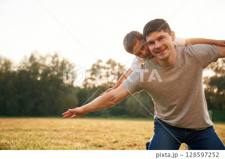 Sitting with hands to the side, imagine the flying. Father and little son are playing and having fun outdoors 128597252