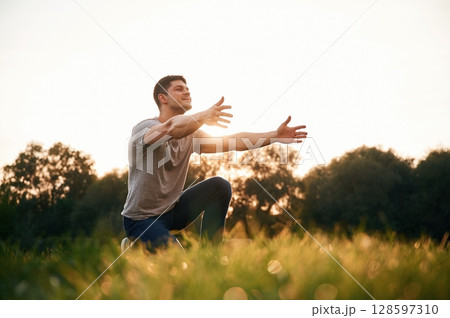 Man in casual clothes is sitting on the ground of field with arms open 128597310