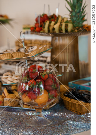 Elegant Dessert Table with Fresh Fruit Display, Pastries, Strawberries, Pineapple, Gold Accents, Silver Tablecloth, Party Buffet Setup. 128597552