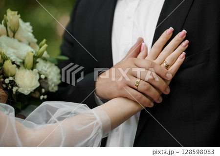 Wedding Rings on Hands of Groom and Bride, Close-Up Shot, White Bouquet, Classic Gold Bands, Marriage, Love, Romance, Formal Attire, Soft Focus Wedding Rings on Hands of Groom and Bride, Close-Up Shot, White Bouquet, Classic Gold Bands, Marriage, Love, Romance, Formal Attire, Soft Focus 128598083