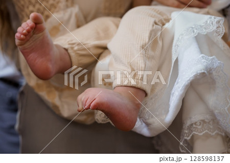 Tender Moment: Mother Holding Newborn Baby's Feet in Beige Clothing, Christening Gown, Lace Details, Soft Lighting, Family, Warmth, New Life. 128598137