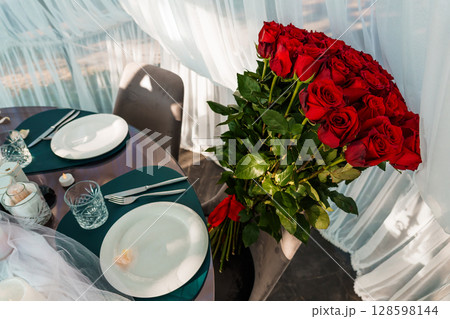 Romantic Valentine's Day Dinner Setup with Red Roses. Intimate Table for Two, Elegant Place Settings, Dark Green Tablecloth, Soft Lighting, and Lush Bouquet Romantic Valentine's Day Dinner Setup with Red Roses. Intimate Table for Two, Elegant Place Settings, Dark Green Tablecloth, Soft Lighting, and Lush Bouquet 128598144