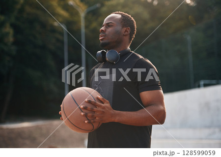 Beautiful sunlight. Young black man is with basketball ball outdoors 128599059