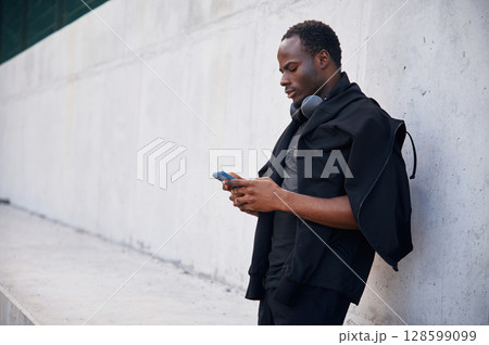 With headphones. Handsome black man is posing outdoors at daytime 128599099