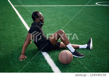 Sitting and relaxing. Young black man is with basketball ball outdoors Sitting and relaxing. Young black man is with basketball ball outdoors 128599130