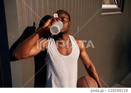 Drinking the water. Young black man is with basketball ball outdoors Drinking the water. Young black man is with basketball ball outdoors 128599159
