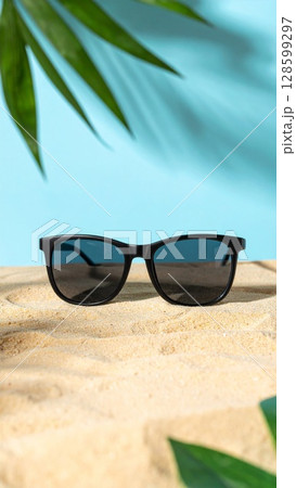 Black Sunglasses on Sandy Beach with Palm Leaf Shadows 128599297