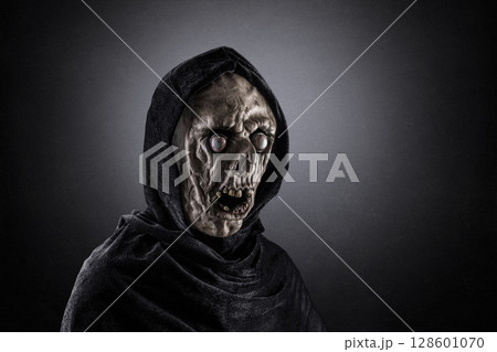 Portrait of a zombie with hooded cape over dark misty background 128601070